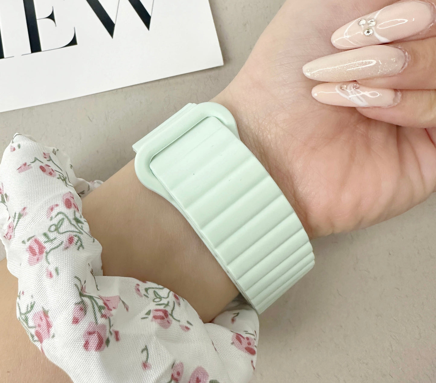 Hand wearing a light green wristband on a neutral background