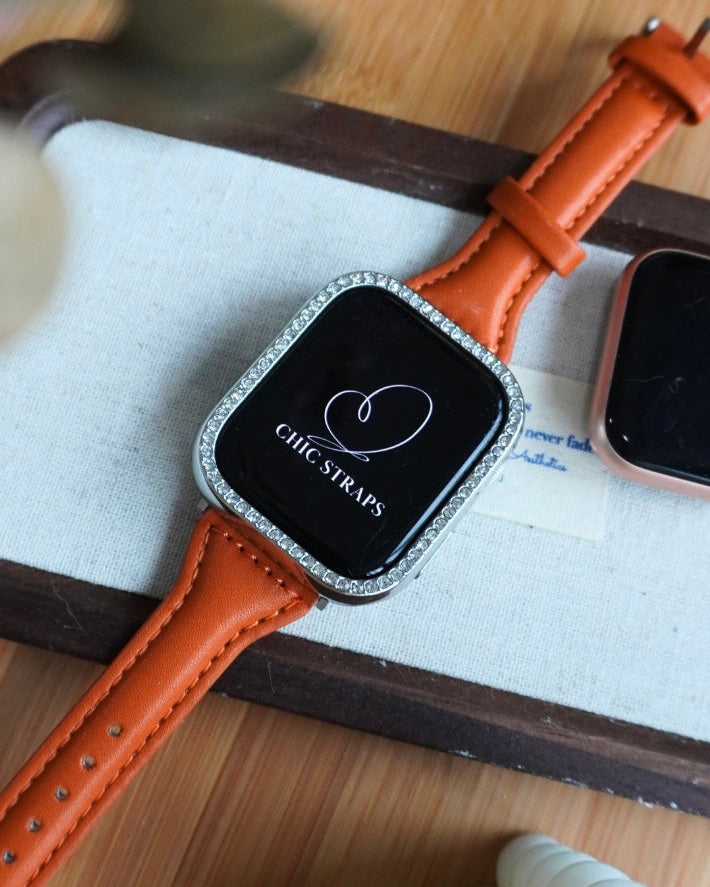 An orange Lucey Strap for Apple Watch displayed on a wooden surface, showcasing its full length and fit around a mock-up of an Apple Watch.